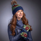 Woman wearing a blue knit hat, scarf, and mittens with highland cow design on a grey background